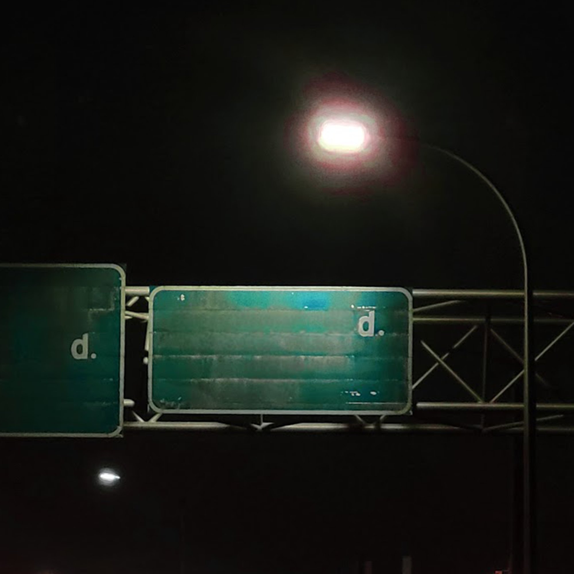 Night photo of green highway signs under a glowing streetlight