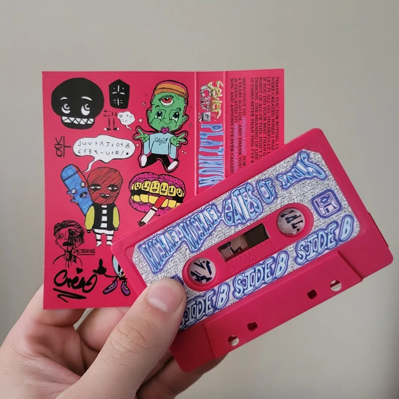 Hand holding the pink Gates of Janus cassette by Crisis Hotline and its sticker-covered J-card