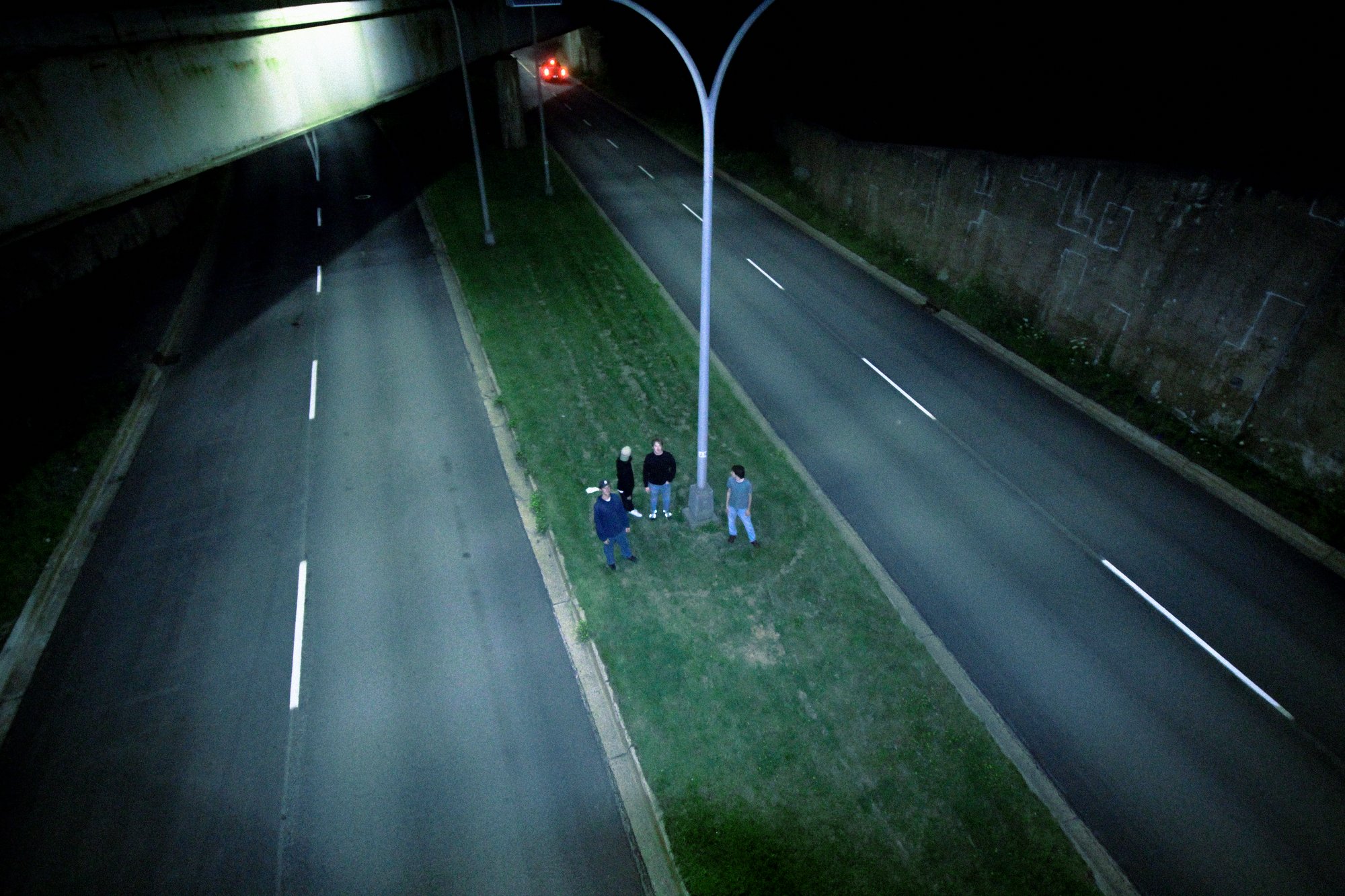 Night photo of people standing on a grass median beside an empty highway under a streetlight