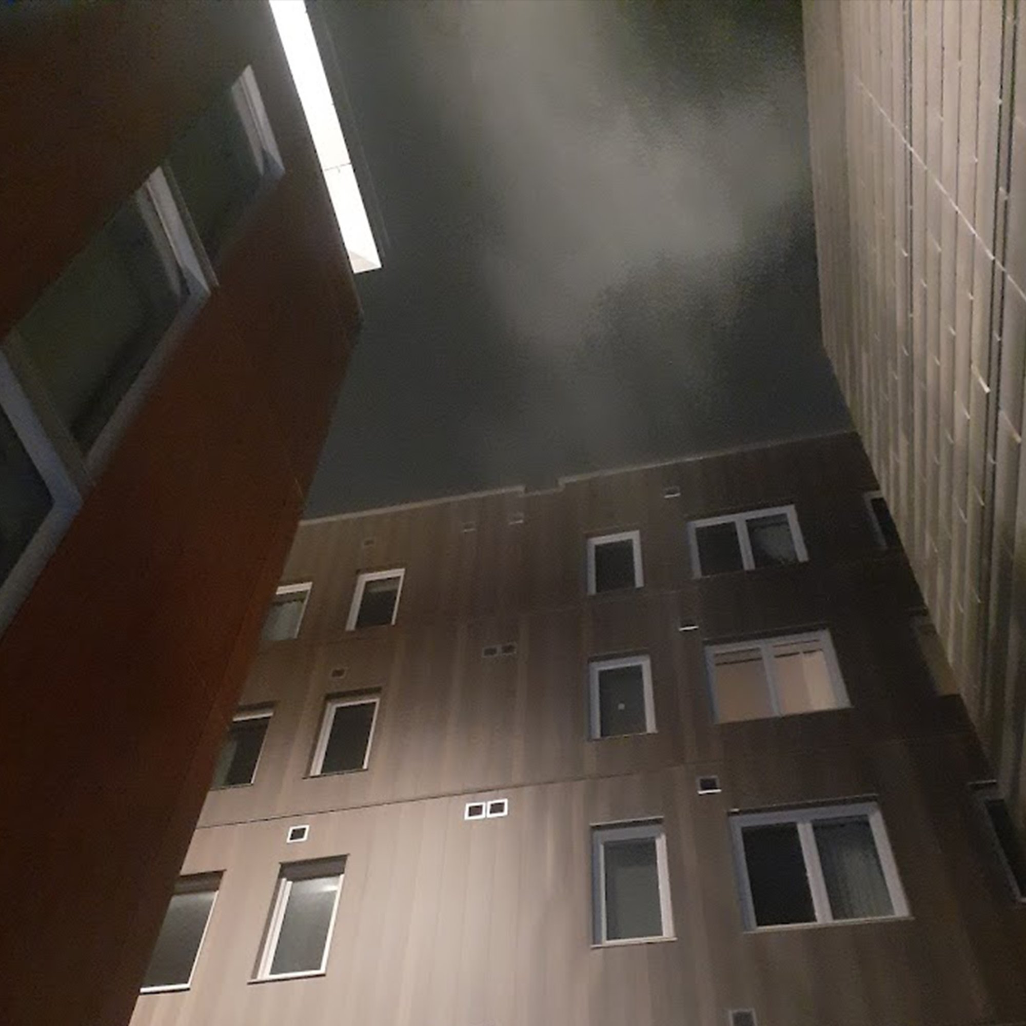 Photo looking up at an apartment building with a bright light and foggy sky